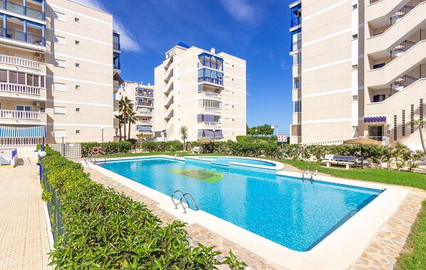 Une piscine entourée d’immeubles d’appartements dotés de balcons, un ciel dégagé et quelques espaces verts.