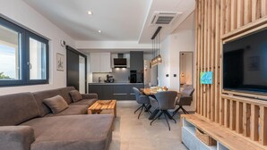 Un soggiorno moderno con divano, tavolo da pranzo e sedie, una cucina sullo sfondo e una TV montata su una parete in legno.
