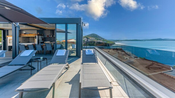 Una terrazza panoramica moderna con poltrone lounge, angolo cottura e vista sul mare.