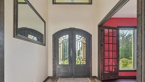 A hallway with a dark wooden floor, a large mirror on the left, and a double door with decorative glass panels. - Lovely studio with AC in charming College Station (College Station)