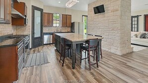 A modern kitchen with a central island, wooden cabinets, and a stone accent wall. - Lovely studio with AC in charming College Station (College Station)