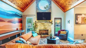 Una sala de estar acogedora con chimenea de piedra, techo de madera y un ventanal grande.