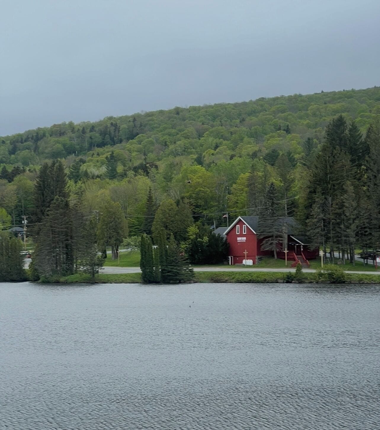 A red cabin by a lake surrounded by dense forest.