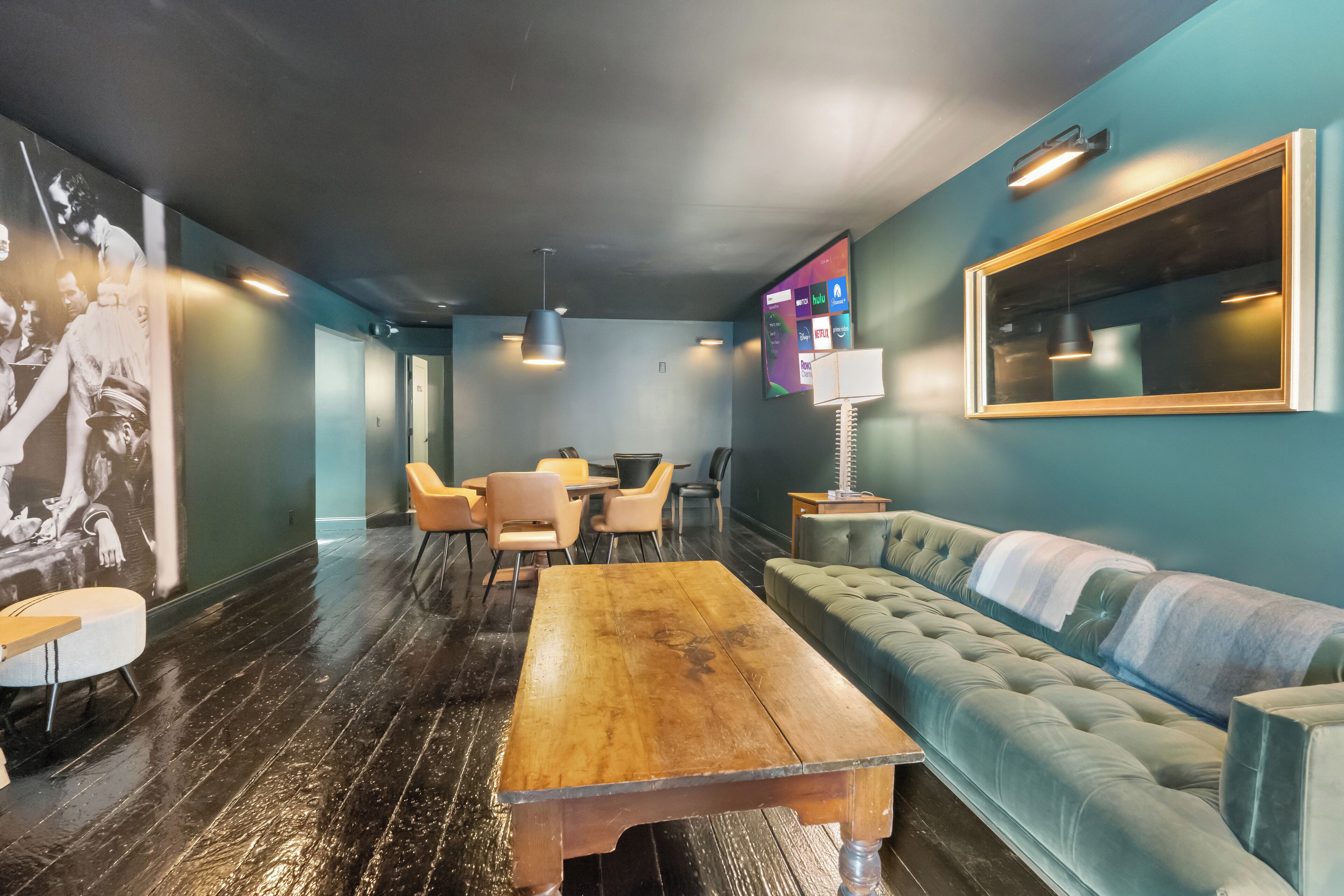 Un salón moderno con una mesa de madera, asientos acolchados y una pantalla de televisión grande.