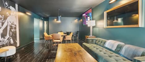 Un salón moderno con una mesa de madera, asientos acolchados y una pantalla de televisión grande.
