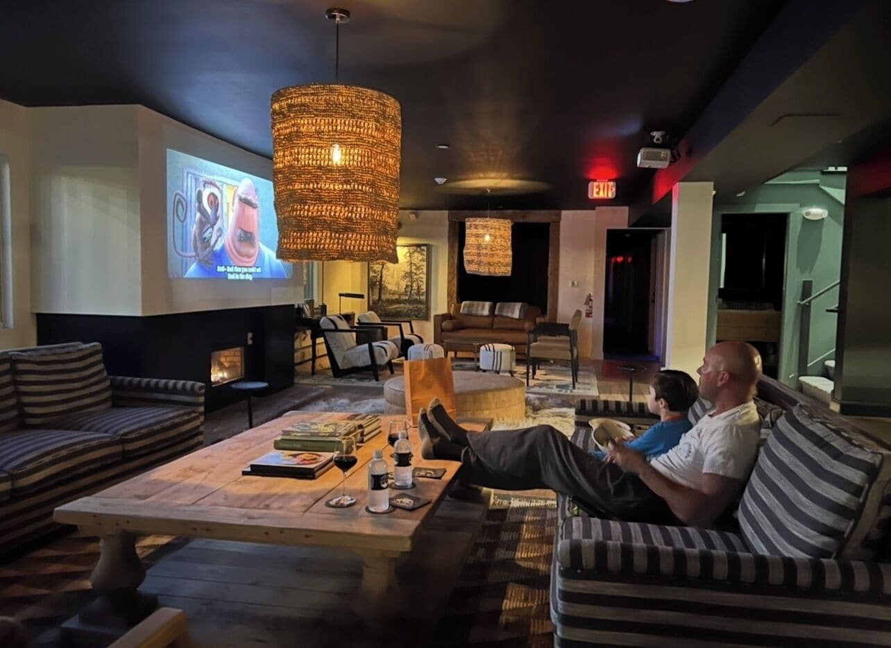 A lounge area with a large screen displaying a movie, a fireplace, and a seating area with striped sofas and a coffee table.