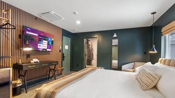 Une chambre d’hôtel avec un grand lit, un bureau avec un ordinateur, un téléviseur fixé au mur et une fenêtre donnant sur des arbres.