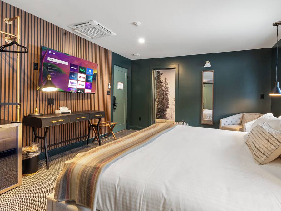 Une chambre d’hôtel avec un grand lit, un bureau avec un ordinateur, un téléviseur fixé au mur et une fenêtre donnant sur des arbres.