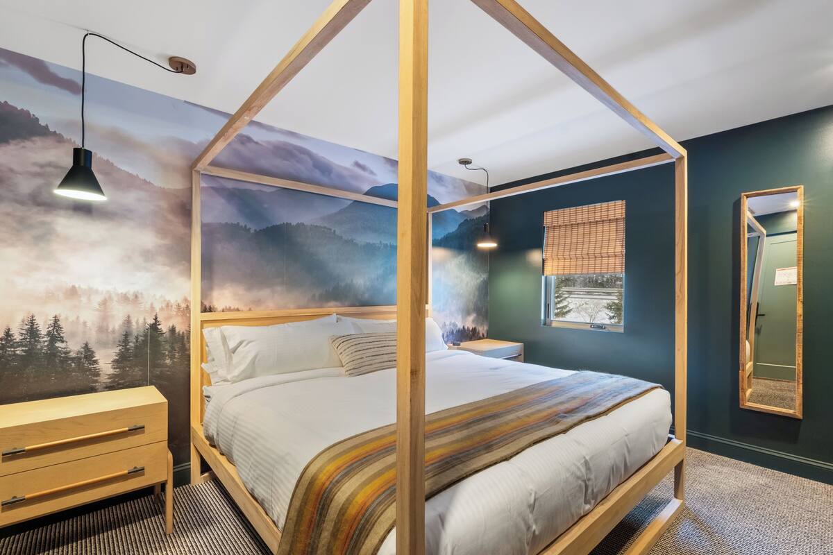 A bedroom with a four-poster bed, wooden nightstands, a wooden dresser, and a large wall mural of a forest.