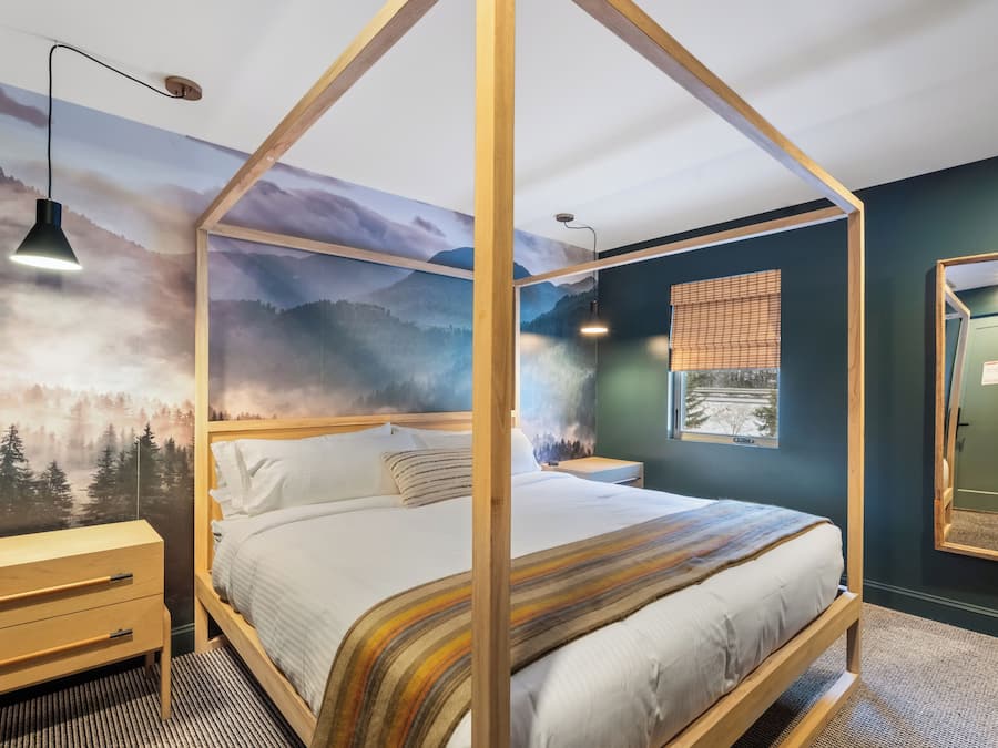 A bedroom with a four-poster bed, wooden nightstands, a wooden dresser, and a large wall mural of a forest.