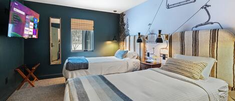 A hotel room with two beds, a TV mounted on the wall, a window with blinds, and a ski lift image on the ceiling.