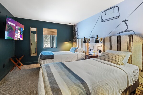 A hotel room with two beds, a TV mounted on the wall, a window with blinds, and a ski lift image on the ceiling.