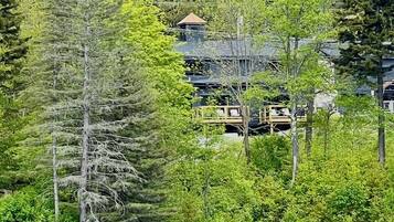 A cabin with a deck overlooking a river, surrounded by dense forest.
