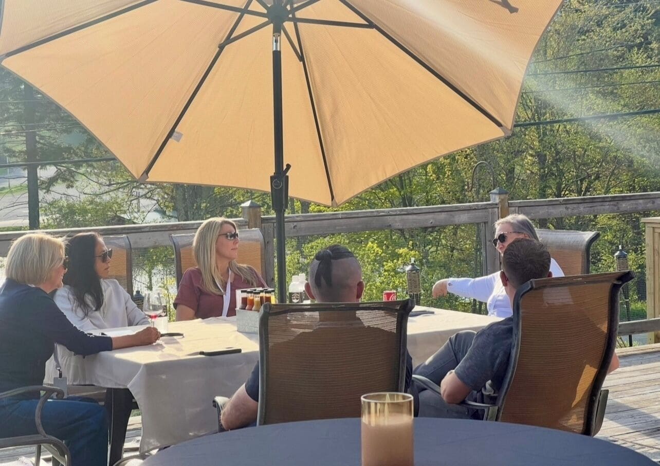 Un grupo de personas cenando en una mesa al aire libre, protegidas por una gran sombrilla.