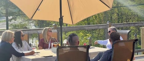 Een groep mensen dineert aan een buitentafel, beschaduwd door een grote parasol.
