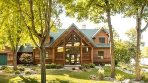 A log cabin with a triangular roof, large windows, and a well-maintained lawn.