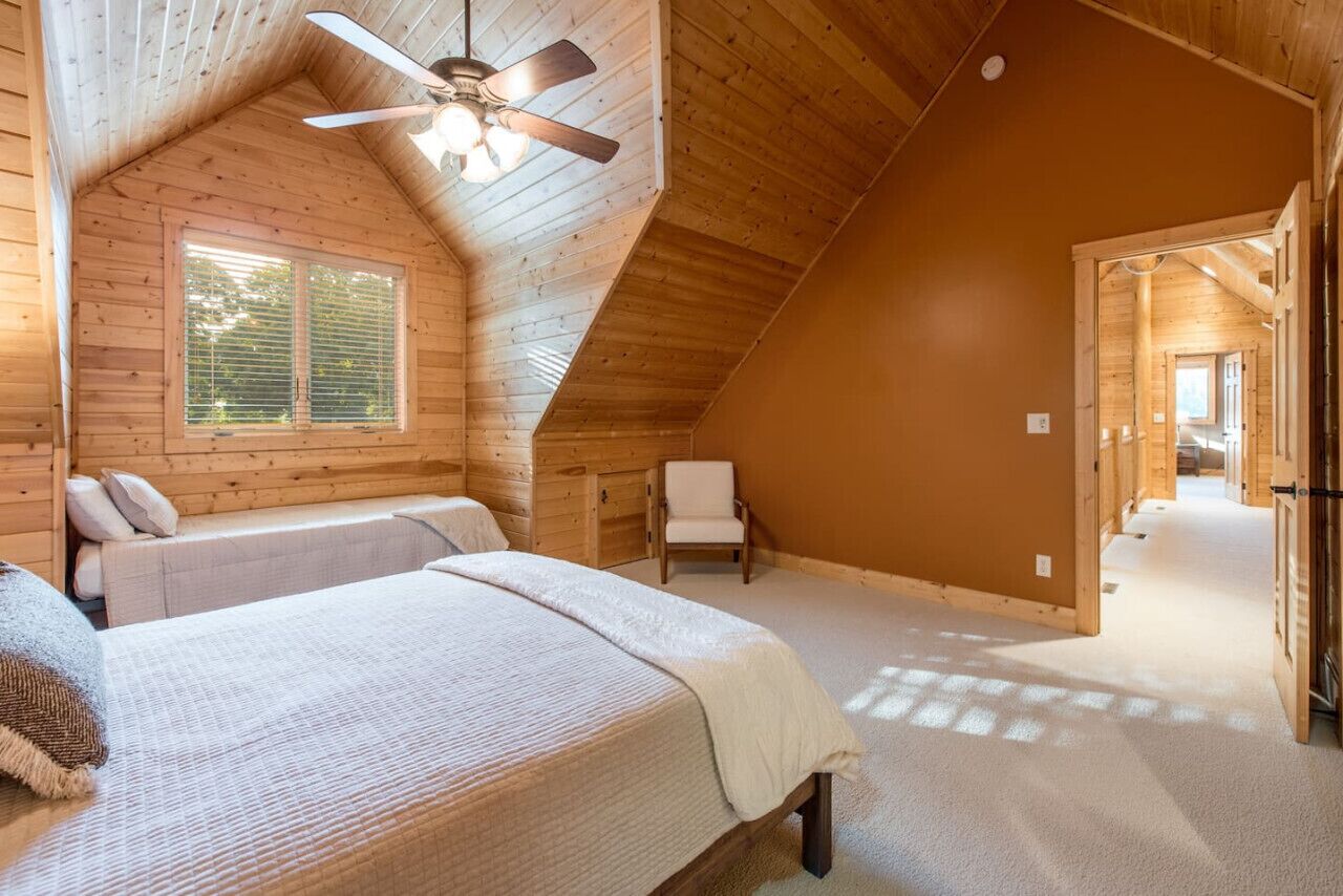 Un dormitorio acogedor en el ático con dos camas, un ventilador de techo y una ventana.
