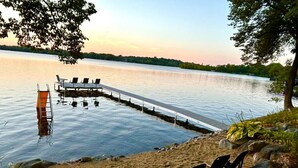 A lakeside deck with chairs and a ladder leading into the water, surrounded by natural scenery.