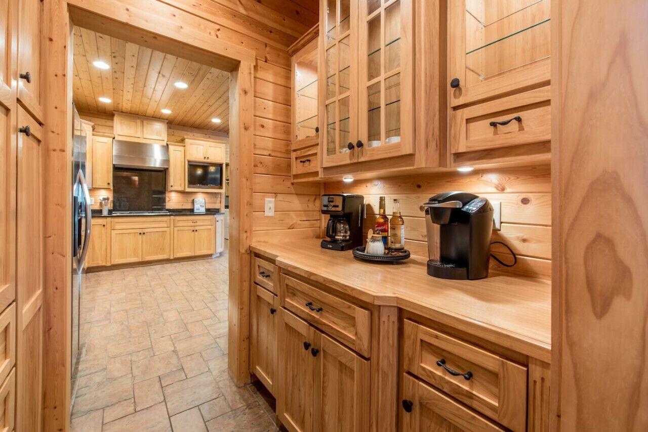 Une cuisine en bois avec un sol en pierre, des placards en bois, un réfrigérateur en acier inoxydable, une machine à café et un grille-pain.