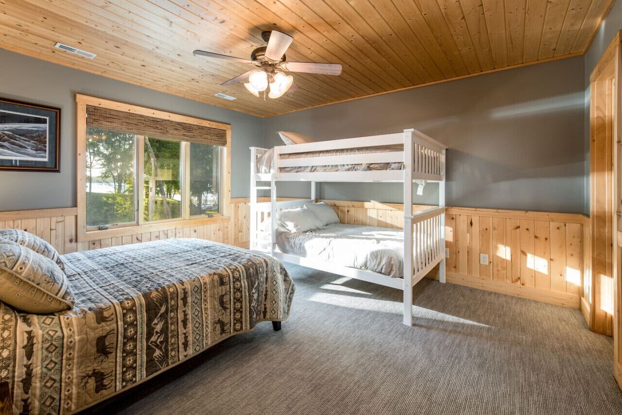 Ein Schlafzimmer mit Etagenbett, Einzelbett, Deckenventilator und großem Fenster.