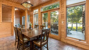A wooden interior with a dining table, chairs, and large windows.
