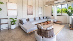 A modern living room with a sectional sofa, a wicker chair, a coffee table, and a large window with curtains. - Blanco Mar Ocean view (Cóbano)