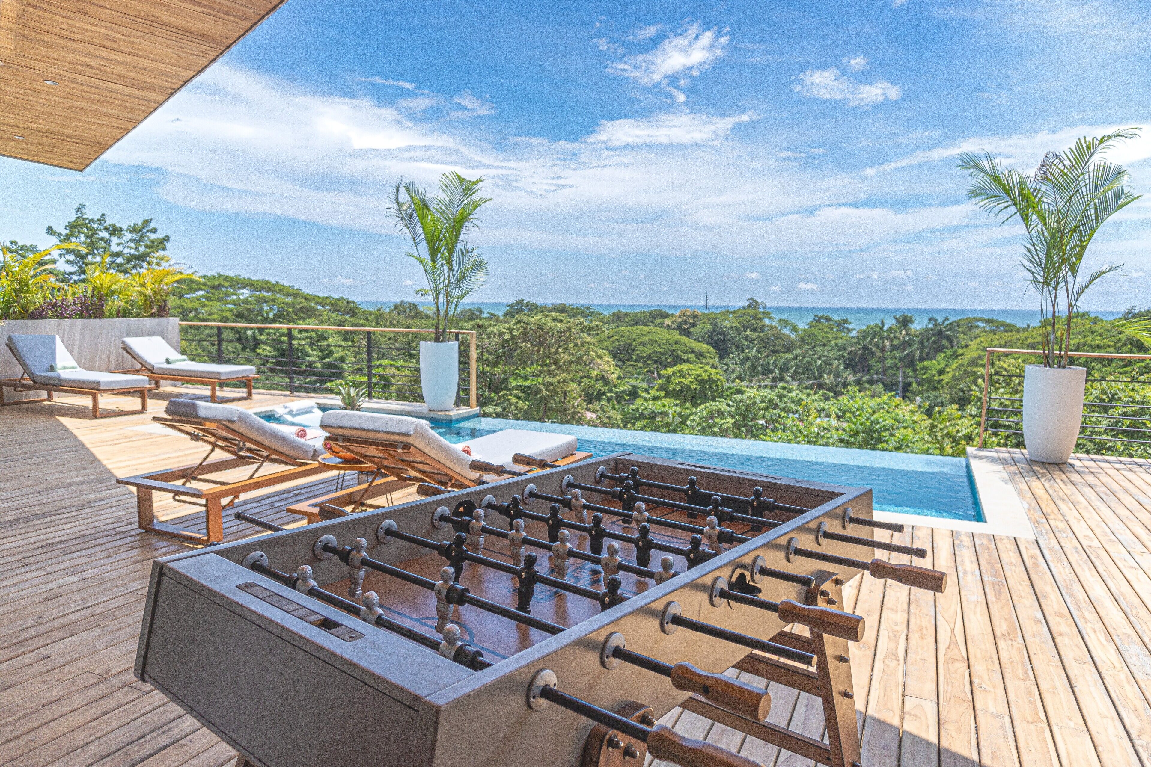 A pool table and lounge chairs on a wooden deck with a view of the ocean.