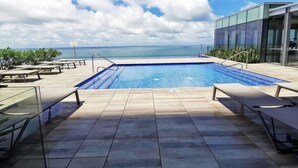 A swimming pool with a view of the ocean, surrounded by lounge chairs and a modern building. - Your Perfect Getaway! Daily Rental in Apartment H2 2305 Seafront (Cartagena)