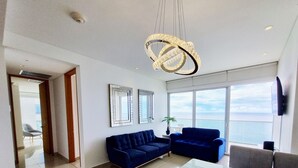 A modern living room with a blue sofa, a glass coffee table, and a large window offering a view of the sea. - Your Perfect Getaway! Daily Rental in Apartment H2 2305 Seafront (Cartagena)