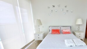 A modern bedroom with a large bed, two nightstands, and a window with blinds. - Your Perfect Getaway! Daily Rental in Apartment H2 2305 Seafront (Cartagena)