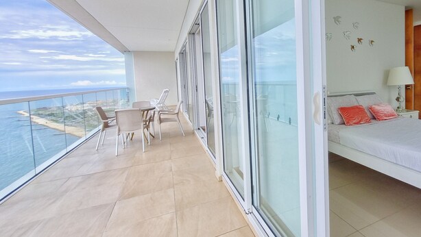 A balcony with a view of the sea, a dining area with chairs, and a bedroom with a bed and pillows. - Your Perfect Getaway! Daily Rental in Apartment H2 2305 Seafront (Cartagena)