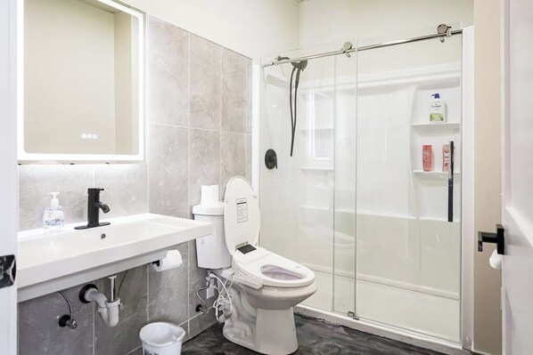 Un baño moderno con inodoro, lavamanos y ducha con mampara de vidrio.