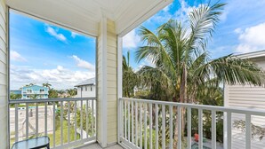 Un balcon avec vue sur une piscine, des palmiers et les maisons voisines.