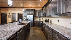 A spacious kitchen with granite countertops, stainless steel appliances, and dark wooden cabinets.
