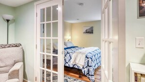 Un dormitorio con cama, una silla, una lámpara y un cuadro en la pared.