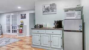 Una cocina moderna con armarios blancos, un refrigerador de acero inoxidable y un microondas. Hay una cafetera en la encimera y una alfombra en el suelo.