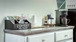 Una encimera de cocina con una estación de café, incluyendo un cartel que dice 'COFFEE? Yes, please!' y diversos artículos relacionados con el café.