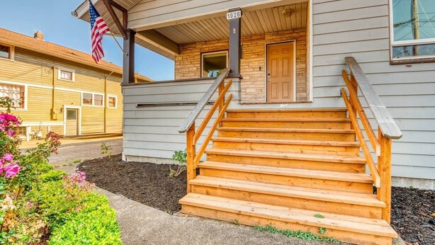 Una casa de dos pisos con una escalera de madera que lleva a la puerta principal, un pequeño porche y una bandera estadounidense.