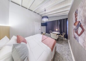 Ein Hotelzimmer mit einem Bett, einem Schreibtisch mit Stühlen, einer Kristallleuchtre und einem Gemälde an der Wand.