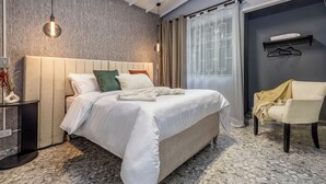 Un lit bien fait, avec une couette blanche et des oreillers, une table de chevet ornée d’un vase et d’une lampe, et une chaise avec une couverture.