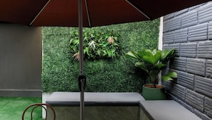 Un espace extérieur moderne, aménagé avec un sol en gazon synthétique vert, un banc rembourré gris et un mur végétal vertical.