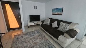 Een moderne woonkamer met een bank, een flatscreen televisie, een salontafel en een kamerkleed met een patroon.