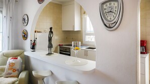 Una cocina moderna con armarios blancos, una isla central con taburetes de bar, una estatua decorativa y un reloj montado en la pared.
