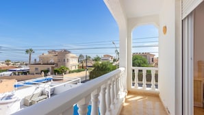 Balcón con piscina, baranda blanca y vistas a casas vecinas y palmeras.