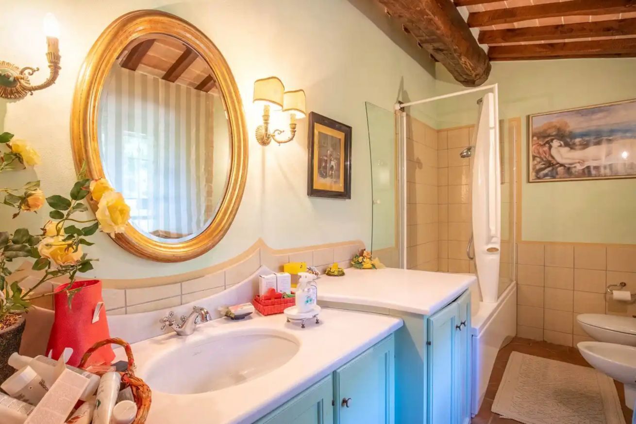 Casa de banho com um espelho grande, duas sanitas, chuveiro e loiça sanitária.