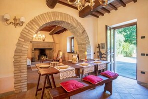 Un comedor con un arco de piedra, mesas de madera con manteles de encaje y cojines rojos.