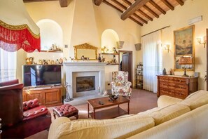 A living room with a fireplace, a television, a sofa, and a decorative chair. - Villa San Vicenzo By MMega (Umbertide)