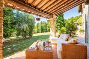 Un patio al aire libre con un sofá de mimbre, una mesa dispuesta con platos y vasos, y una maceta colgante.