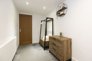 Een gang met een houten deur, een witte radiator, een houten dressoir en een metalen plank met planten.