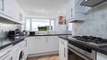 Una cocina moderna con armarios blancos, lavadora integrada, estufa y ventana con vistas al exterior.
